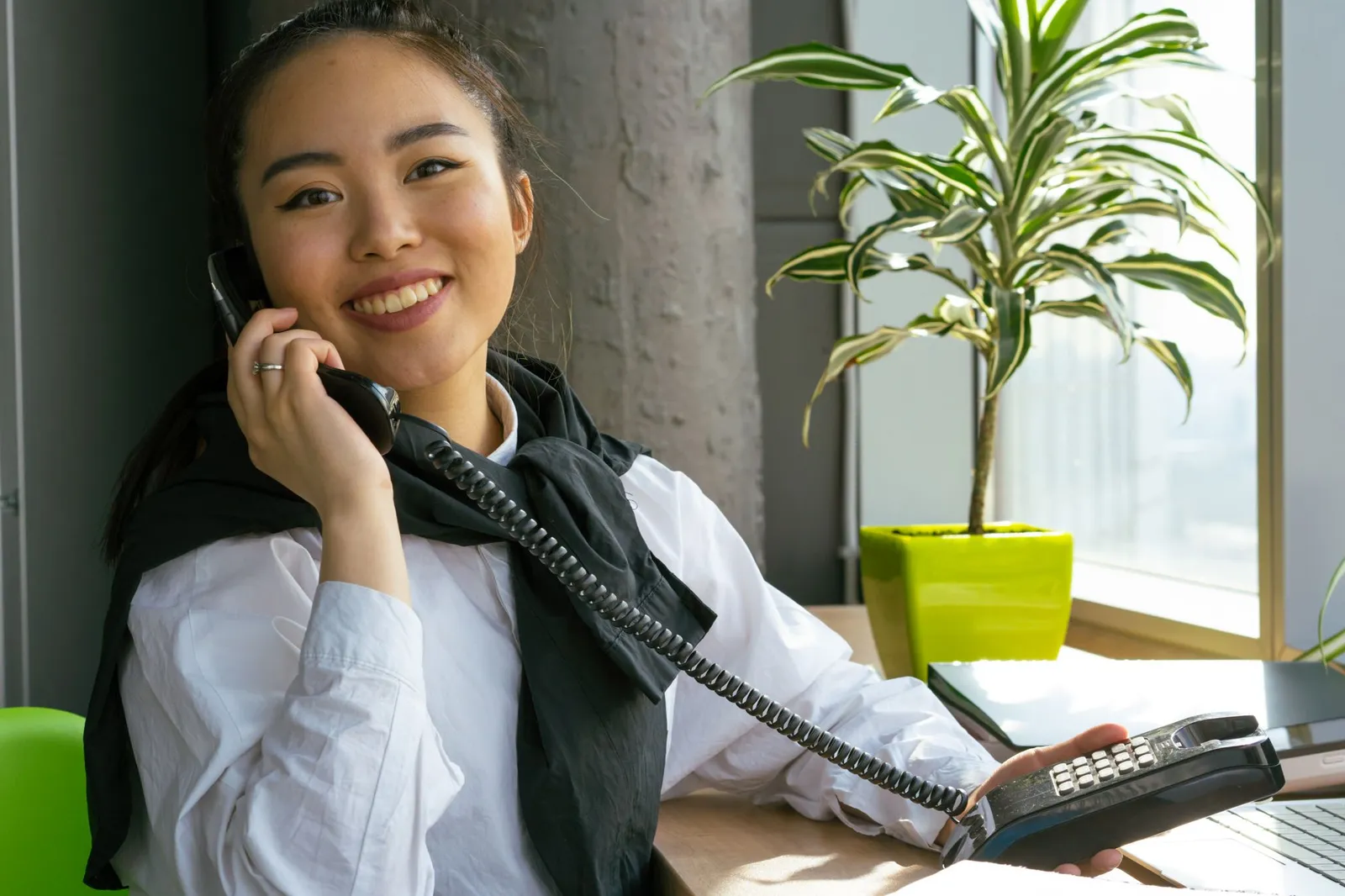 A smiling office worker answers a landline phone at her desk