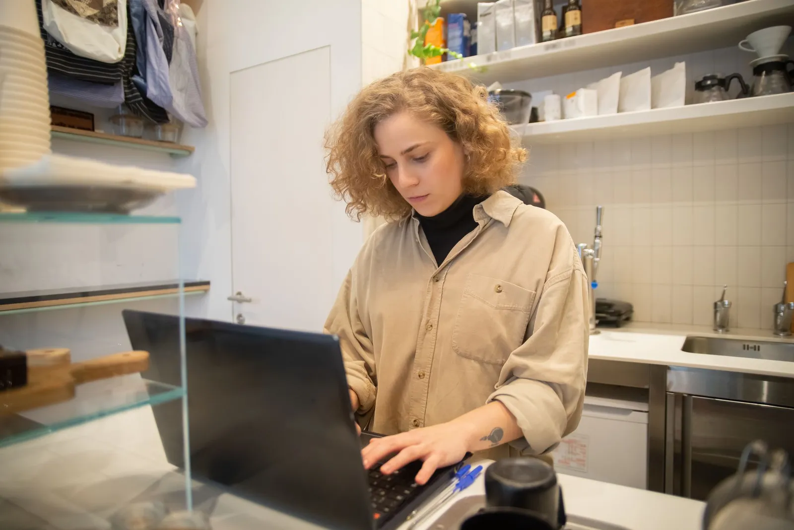 A small business owner works on a laptop behind the counter of her shop