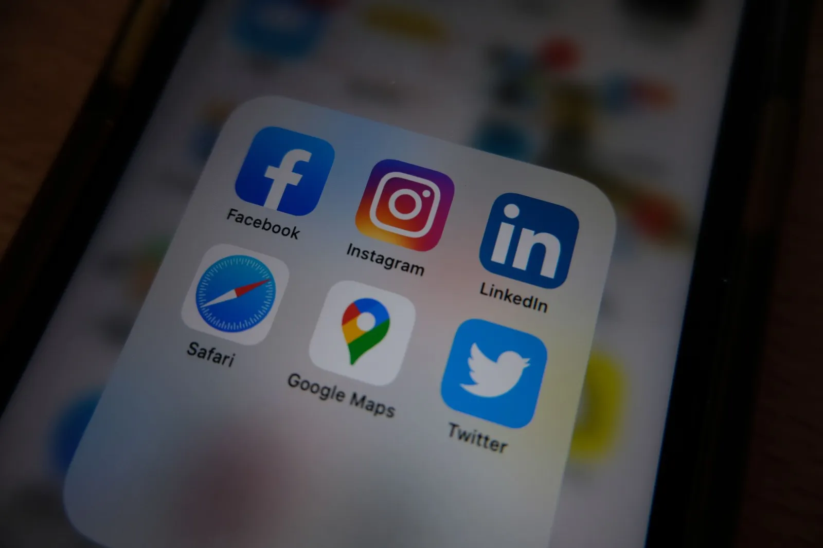 A smartphone screen showing a folder of apps including Facebook, Instagram, LinkedIn, Twitter, Safari, and Google Maps