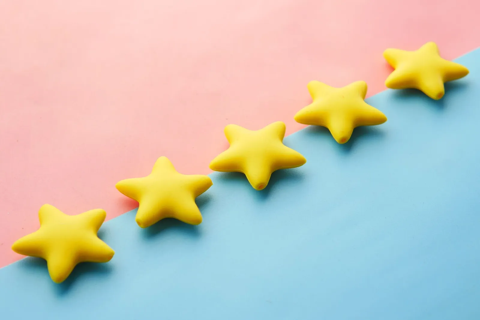 Five yellow star-shaped objects arranged diagonally across a pink and blue background, representing a five-star review
