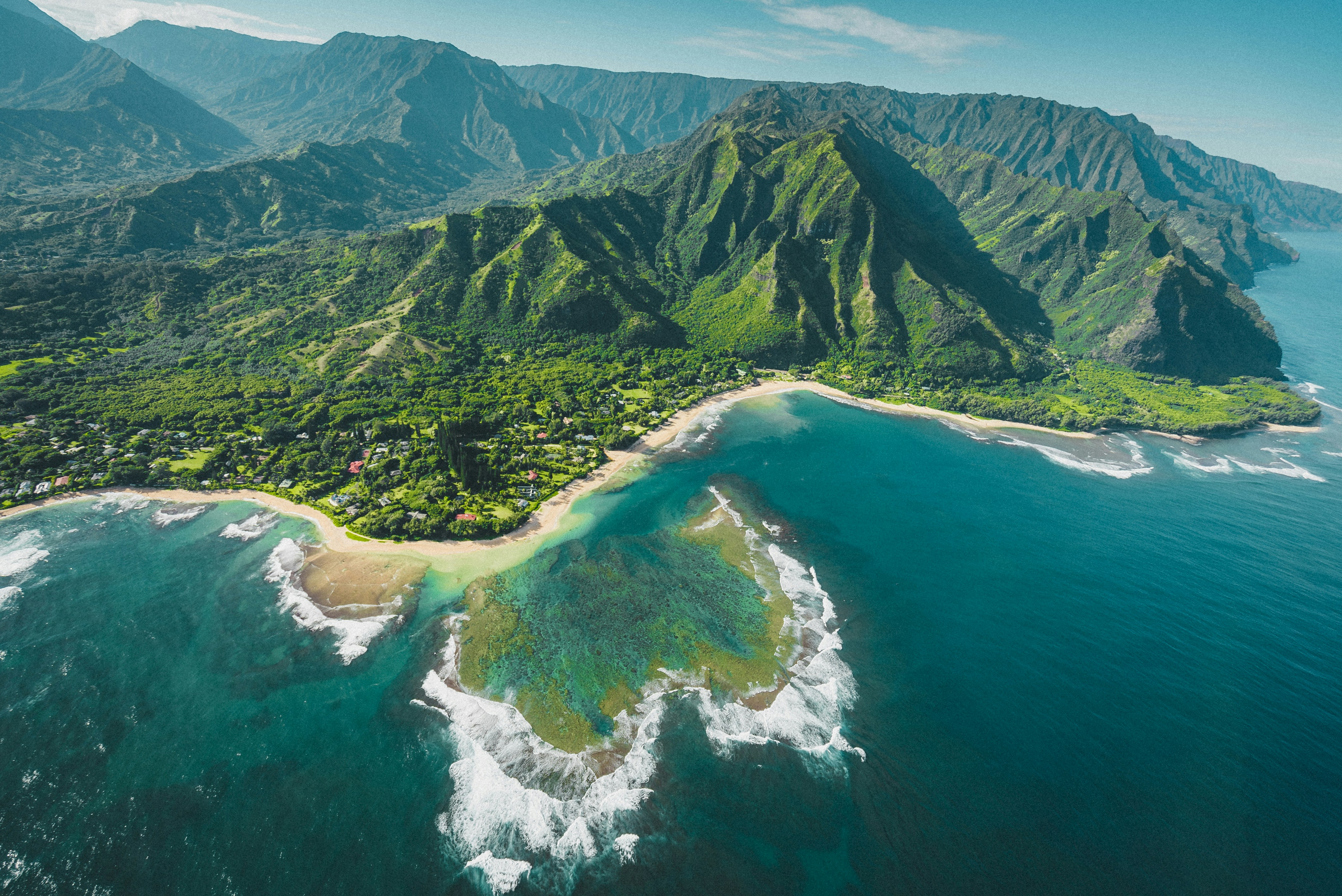 An aerial view of a lush green coastline with mountains and a coral reef