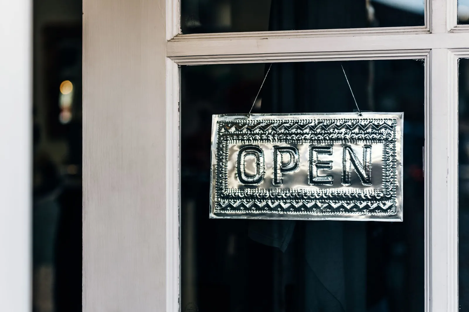 A metal OPEN sign hangs by a chain in the glass door of a small shopfront