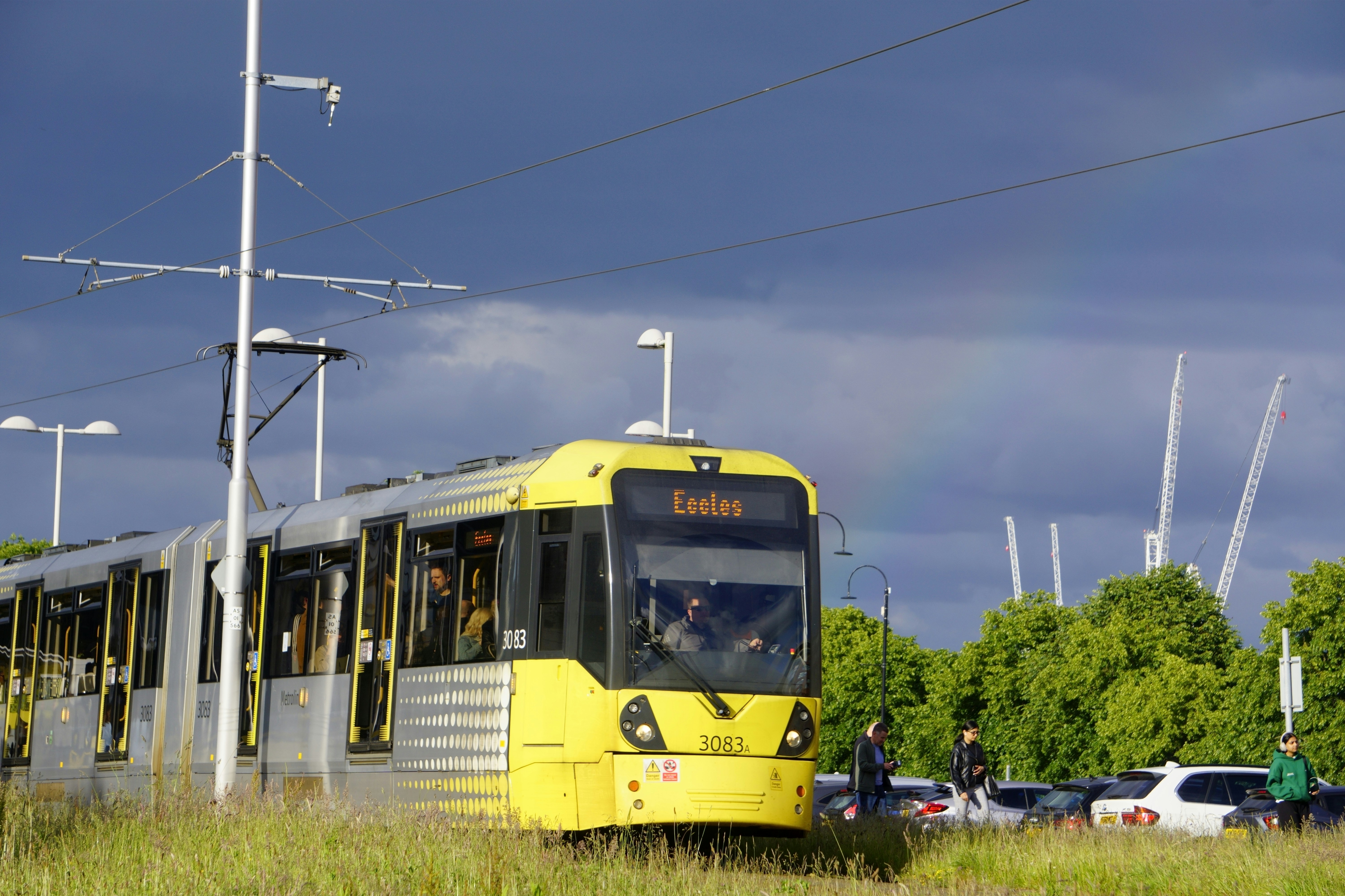 A yellow train traveling down train tracks next to tall grass