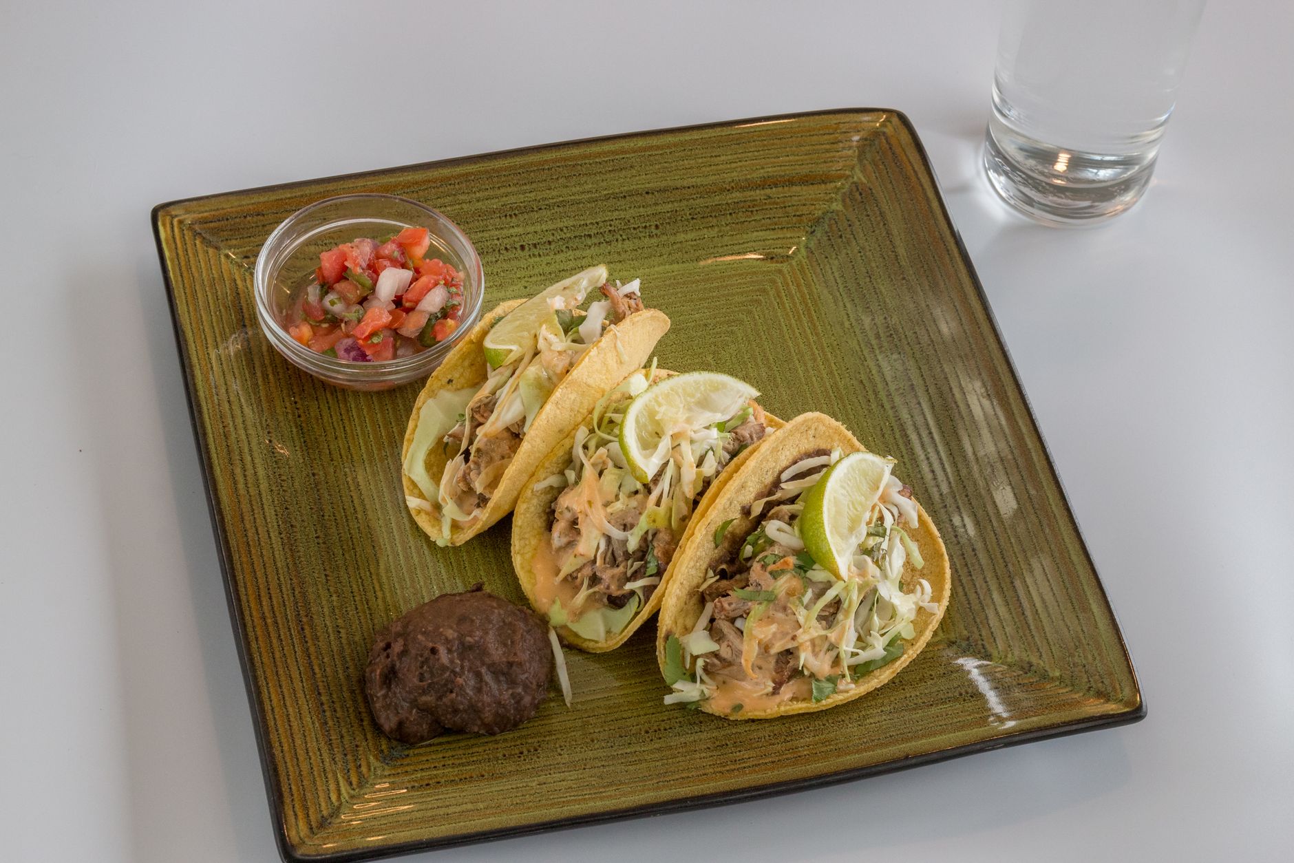 Close-up of freshly prepared tacos with salsa and black bean on a square plate, perfect for food enthusiasts.