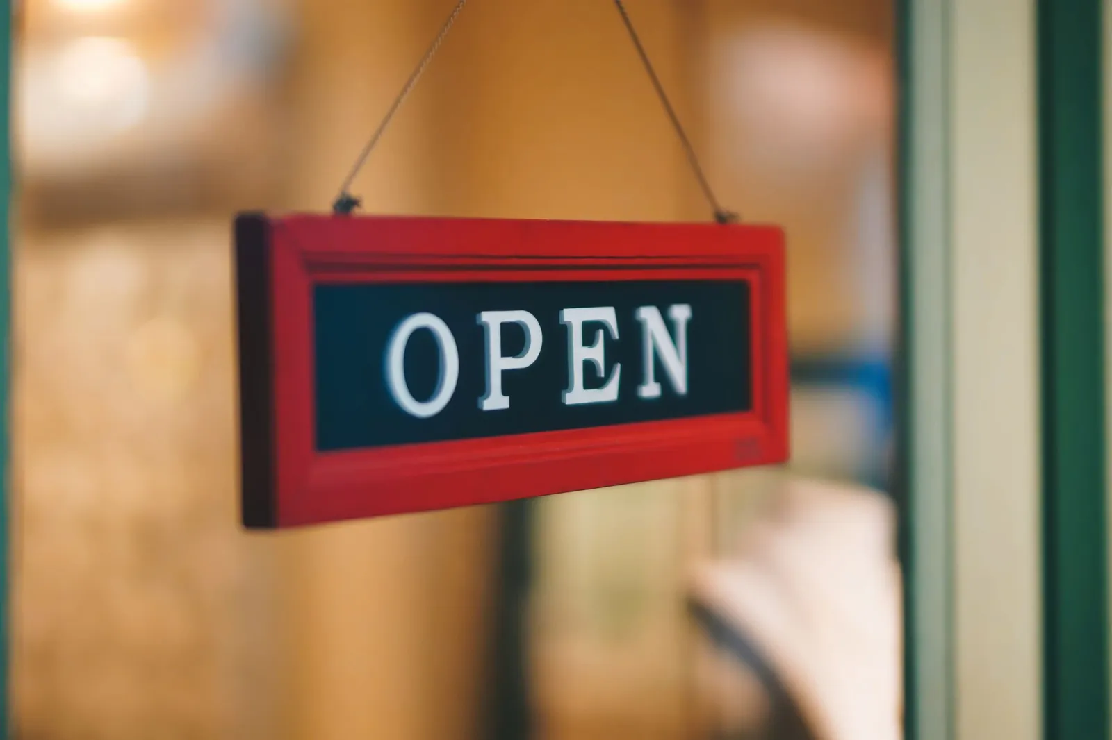 A red OPEN sign hangs by a cord in the glass door of a small shop entrance