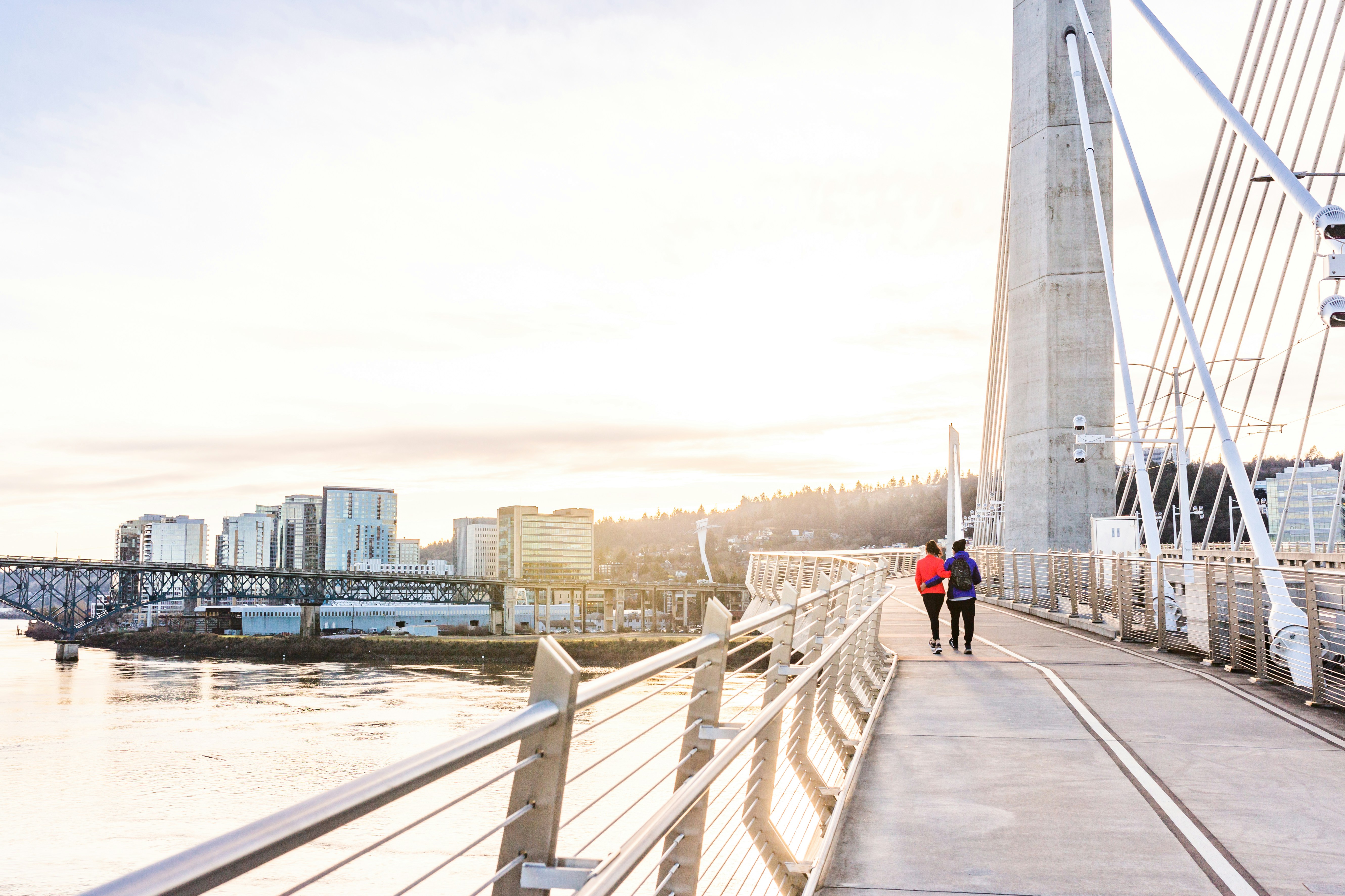 man in red jacket and blue denim jeans walking on gray concrete bridge during daytime