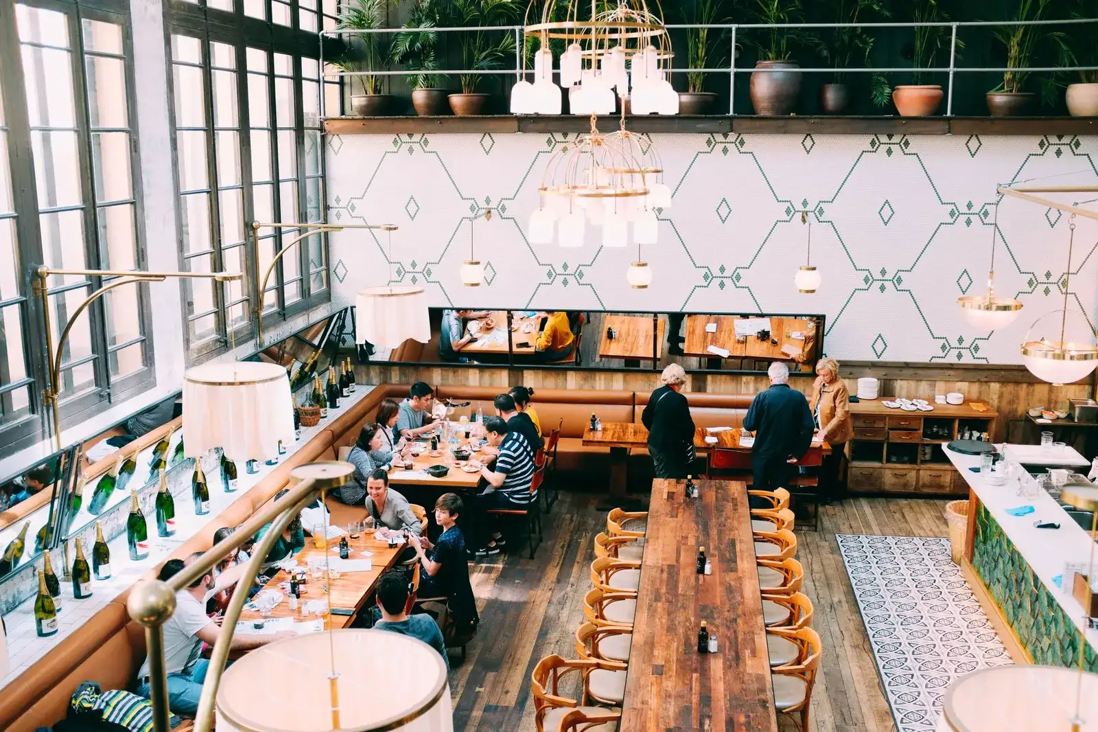 A busy restaurant dining room with wooden tables, pendant lighting, and guests eating together