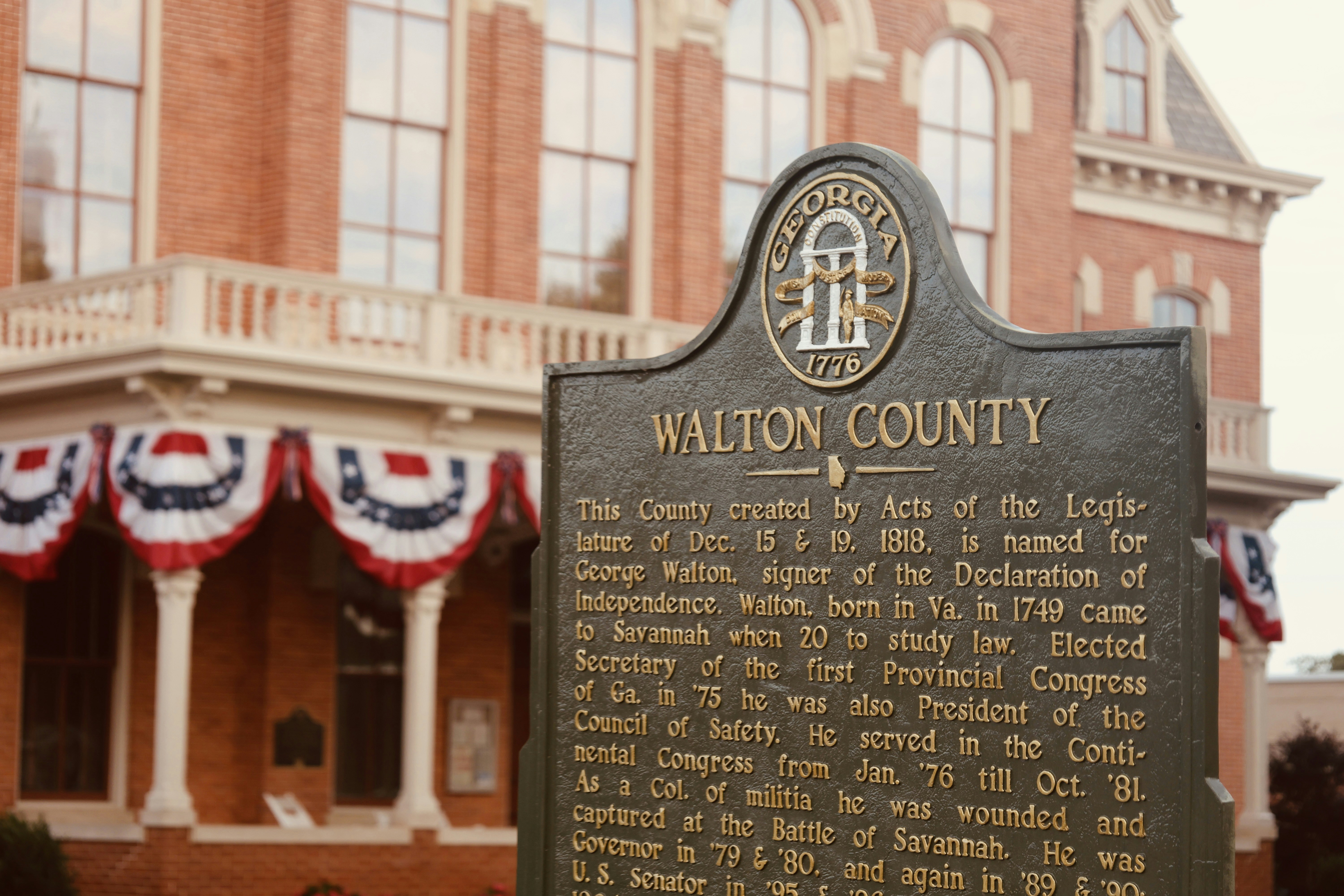 A Walton County historical marker in front of a brick building with patriotic bunting