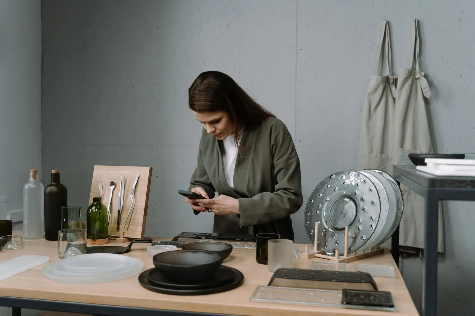 A craftswoman in her workshop uses her smartphone to photograph handmade ceramic pieces she made