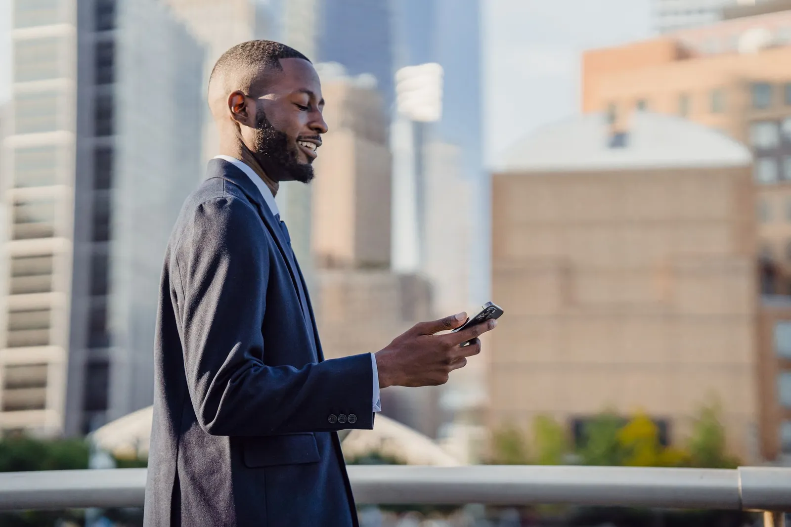 A man in a suit smiles while using his smartphone outdoors in a city